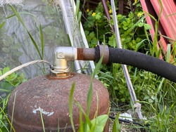 Old rusty pressure vessel, new metal valve and a rubber hose. Faucet and rubber hose fixed with a clamp. Joint of a cylinder, valve and a flexible pipe