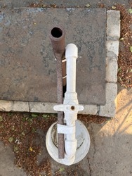 Domestic waterline with gate valve. White plastic pipe for domestic water fixed to a rusty metal bar. Top view of a check valve