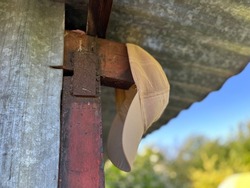 Beige (sandy) headdress (a cap) hanging under aluminium roof. A cotton cap with a visor is the excellent solution to protect your head from direct sunrays in the tropical area