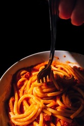 close up of hand with fork twirling Bucatini, spaghetti pasta with red tomato sauce, Italian Cuisine