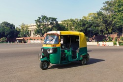 Tuk tuk - traditional indian moto rickshaw taxi on one of the street of New Delhi. yellow green tricycle stands on the square against the background of the presidential Palace. 