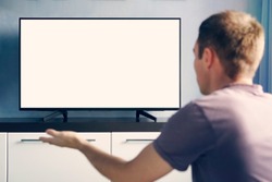 A young guy emotionally watching TV and waving his hands in discontent. Blank white screen for design.
