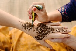 Artist applying henna tattoo on women hands. Mehndi is traditional Indian decorative art. Close-up, overhead view
