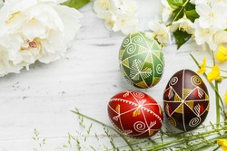 Three handmade Easter eggs decorated with wax-resist dyeing technique. Ukrainian pysanka on white shabby wooden background with empty space for text