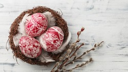 Pysanky, decorated Easter eggs in the nest, pussy willow branches and feathers on white wooden background, wide format, top view, copy space