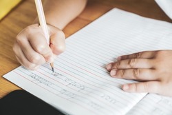 The kid's hand is practicing writing English cursive handwriting sentences in a notebook with a pencil. Cursive handwriting practice.  Kindergarten writing skills. Self-learning. Copy space for text.