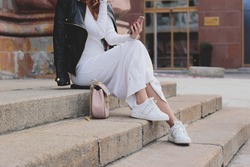 Fashion and style foxy girl in white knitted dress and white sneakers holding her mobile phone and taking self portraits