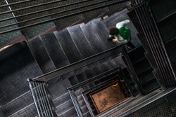 A man walking up the square steel stairwell,view from the top.