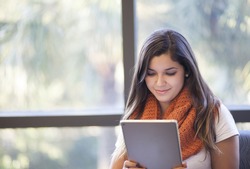 Student engaged with tablet at library. Focused student reading tablet, smiling in the fall, winter