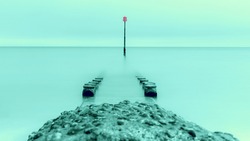 A split toned long exposure image of a groyne and a groyne marker, foreground defocussed image