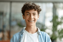 Closeup portrait of smiling smart curly haired school boy wearing braces on teeth looking at camera. Education concept 
