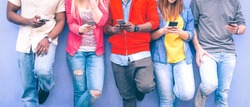 Teenagers texting mobile phone messages leaning on urban wall - Group of multiracial friends using cellular standing outdoors - Concept of students addiction to social network and telephone technology