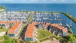 Aerial drone view of typical modern Dutch houses and marina in harbor from above, architecture of port of Volendam town, North Holland, Netherlands