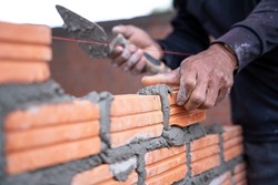 A hand of construction worker, industrial bricklayer installing bricks on construction site.