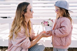 Adorable beautiful little girl wears cap and sunglasses gives mom a bouquet outdoor. Celebration mood, happy emotions, mother's day, birthday, spring, fresh flowers 