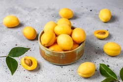 bowl of fresh ripe apricots with leaves, Delicious ripe apricots in a wooden bowl on marble table close-up. top view from above, Ripe apricots and apricot leaves, apricot cut in half and sl