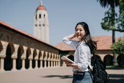 asian college girl standing outdoor going to class at school in summer tour program. elegant smart exchange student study overseas in stanford usa. young woman freshman in new semester cheerful smile
