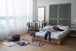modern bright bedroom with messy clothes scatter on white bed and floor. empty room with nobody in cozy apartment. packing luggage suitcase for summer vacation and spring holidays concept lifestyle.