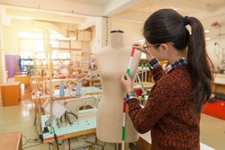 back view angle photo of pretty attractive clothing making company female employee using tape measuring design product with mannequin dummy in fashion studio.
