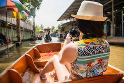 back view photo of elegant beauty girl visiting Damnoen Saduak floating market and using personal camera taking travel picture in Thailand holiday.