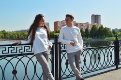 A young girl and a young man in the same clothes on a bridge near the water