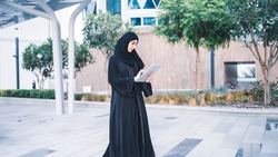 Arab muslim business woman working on tablet in outdoor meeting. Arabian Saudi or Emirati lady businesswoman wearing Abaya 