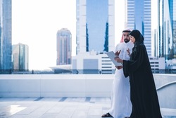 Arab couples or colleagues working together on tablet or laptop wearing traditional clothes and abaya. Muslim employees Saudi or Emirati business woman and man