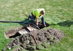 A worker doing routine maintenance pumping out a home septic tank