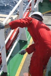crew ship or ordinary seaman is painting and primering railing of outside bridge accommodation with green paint brand jotun. Boatswain use red coverall and safety helmet for daily work