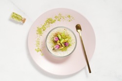 Creamy rice pudding topped with pistachio and cinnamon in a glass bowl on pink plate and marble table. Traditional Turkish dessert sutlac. Minimal bright and airy background.  Copy space. Top view.