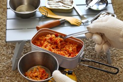 camp food. making a tomato pasta dish in mess tin and serving it.