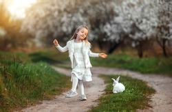 A little girl dances on the road at sunset. Happy childhood. A girl with a rabbit is playing in the meadow.