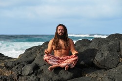 rasta boy meditating in lotus position, by the sea