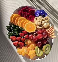Raw Food with variety of cut fruits
(orange, dragon fruits, Strawberry, grapes, kiwi, apple, star fruits, banana.)
 fresh vegetable, and edible flower (Butterfly Pea Flower)
