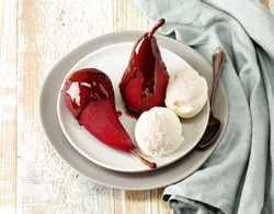 Plate of pears poached in red wine, dessert decorated with melted chocolate and ice cream on wooden table