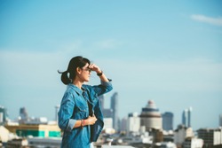 Portrait of a relaxed Asian woman looking forward at the horizon cityscape in the background with her hand on the forehead- copy space