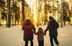 family walking in winter forest at yellow colors sunset