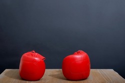 A set of two mild and comfortable red leather boxing gloves are on the light wooden table near a dark grey wall as a background, ready for competition