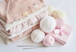 Stack of knitted clothes and balls of yarn, knitting needles, accessories for knitting. Baby clothes. Needlework, hobby, knitting, handwork