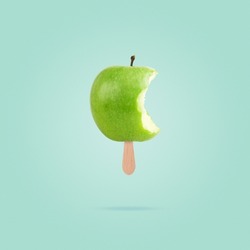 Green bitten apple with ice cream stick on pastel blue background. Diet healthy concept. Creative summer concept.