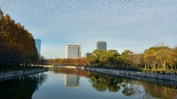 The canal around the Osaka Castle Park. Facing the city area and business buildings. Cloudy blue sky and canal reflection of buildings. Beautiful evening golden sunset light. Osaka, Japan.