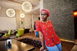 Stylish african woman in red shirt and hat posed indoor cafe.