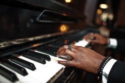 Fingers of african american man in black suit play piano.