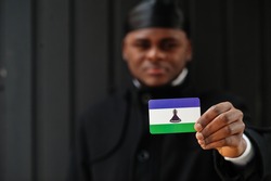 African man wear black durag hold Lesotho flag at hand isolated dark background.