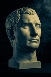 Bronze color gypsum copy of ancient statue of Guy Julius Caesar Octavian Augustus head for artists on dark textured background. Renaissance epoch. Plaster sculpture of man face.Template for art design