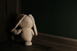 Plush bunny is sitting in the corner of the dark room. Child abuse and punishment concept.