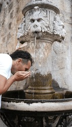 Man drinking water from old historic stone fountain  with carved lion head Dubrovnik, Croatia