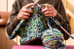 A woman knits from thick yarn. Handmade clothes. The girl sits on the couch and goes in for her hobbies. Knitting close up.