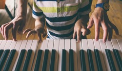 A woman teaches her son to play the piano. The boy masters the keyboard musical instrument. A child learns music. Children's and women's hands on the piano keys. Music lesson. Tutor for a child.