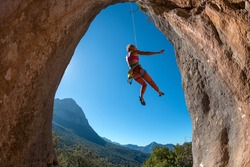 Rock climber descends from the route, the climber hangs on a rope, a rock in the form of an arch, climbing routes in a cave, a girl rides on a rope